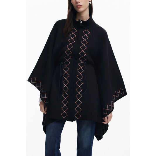 Black poncho with red geometric patterns worn by a person on a white background