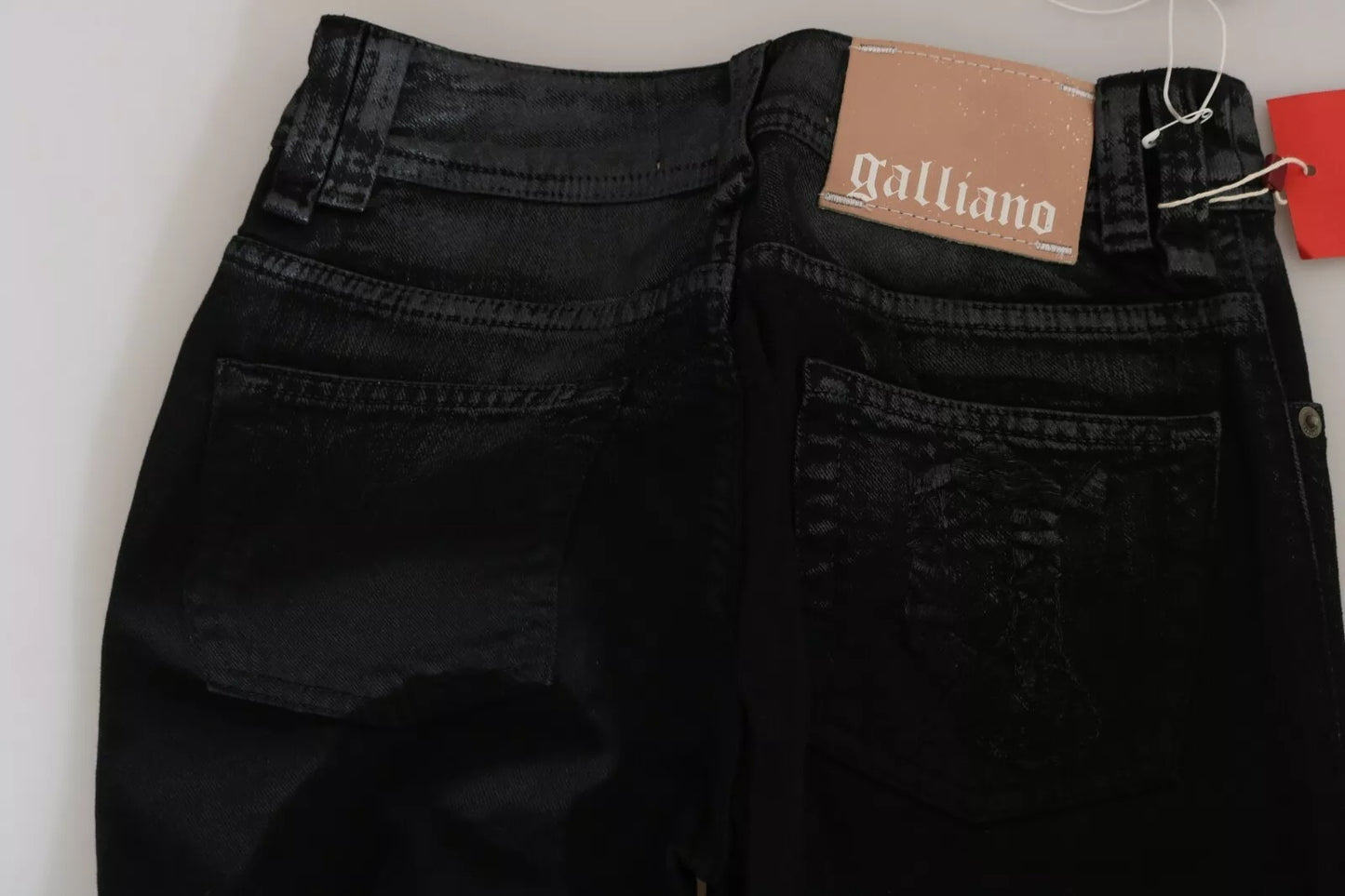Black jeans with a Galliano tag on a white background